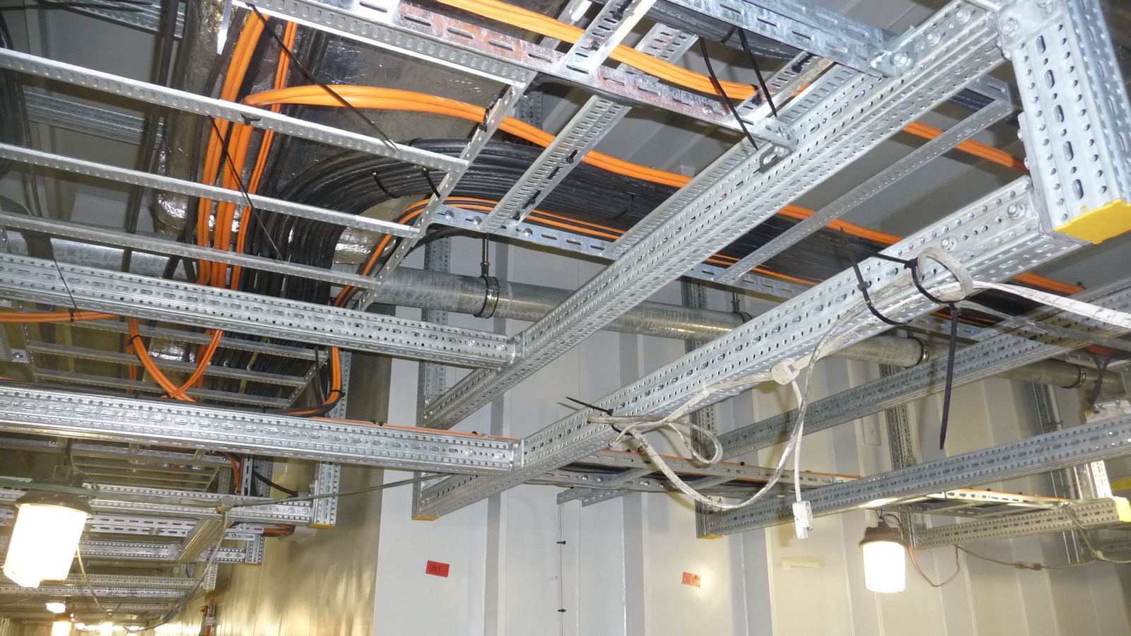 Bandejas portacables de escalera y perforadas de acero galvanizado con cables eléctricos naranjas y negros en un techo técnico