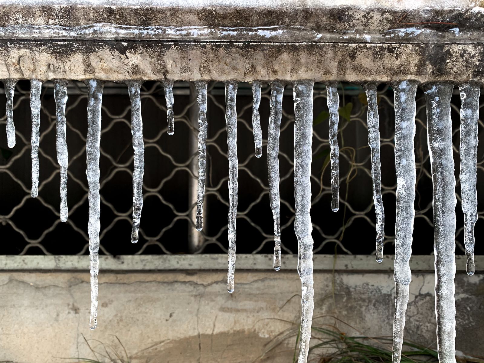 Carámbanos de hielo colgando de una barra metálica junto a una reja en un día de helada
