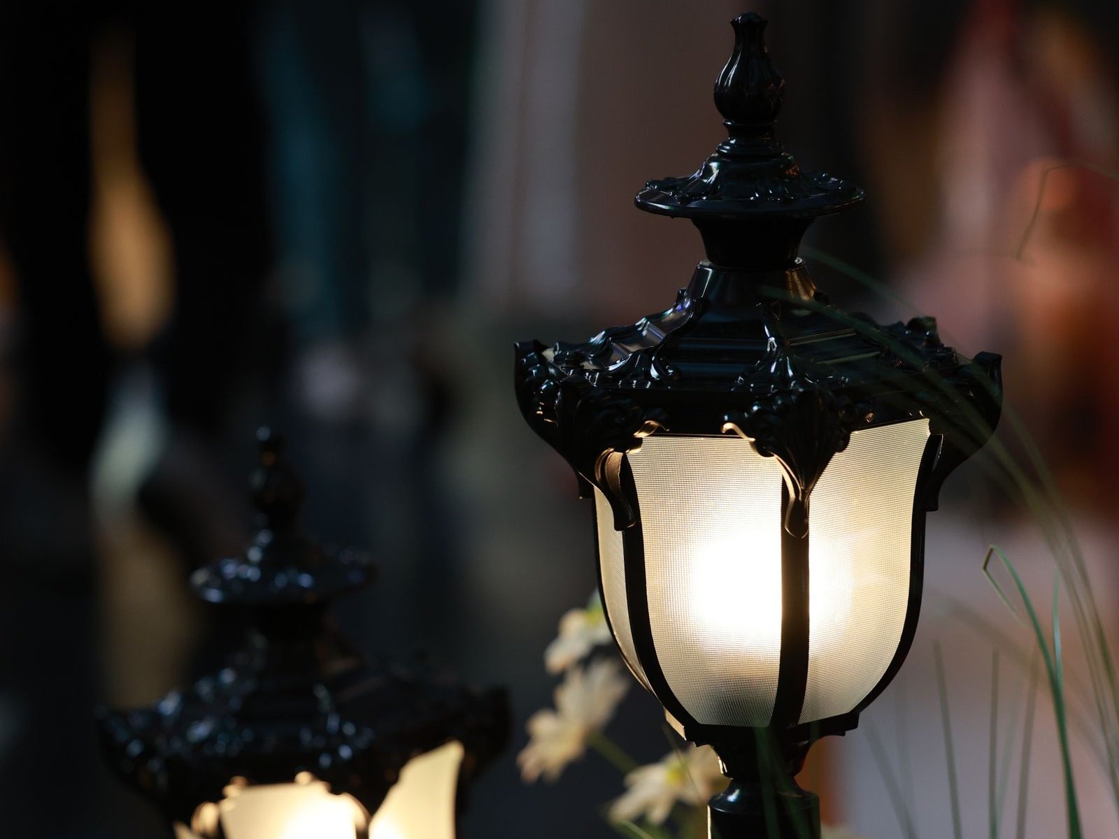 Dos farolas bajas de jardín encendidas al anochecer entre hierbas y flores blancas