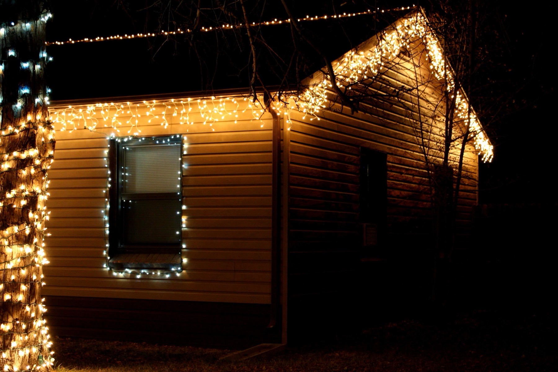 Fachada de una casa con guirnaldas de luces de Navidad blancas en el alero y alrededor de la ventana, de noche