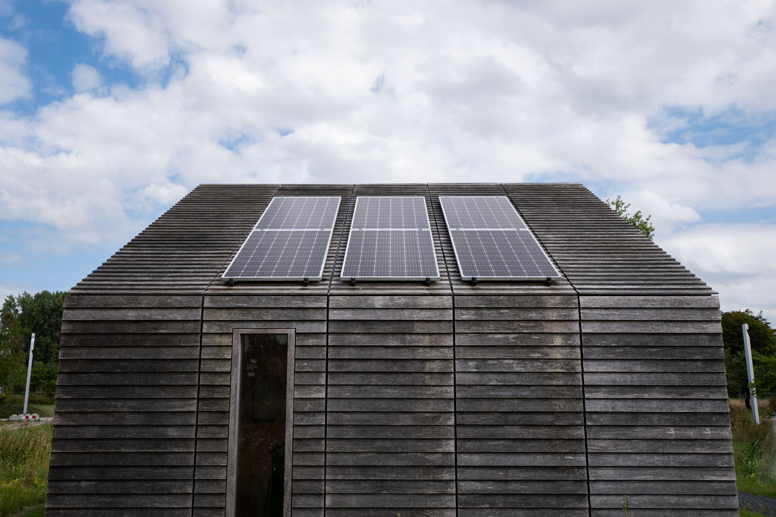 Cabaña de madera en el campo con tres placas solares en el tejado bajo un cielo con nubes
